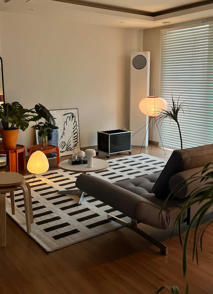 Modern living room with white walls and brown wood flooring, featuring a gray sofa bed and black-and-white geometric rug centrally placed creating a cozy atmosphere