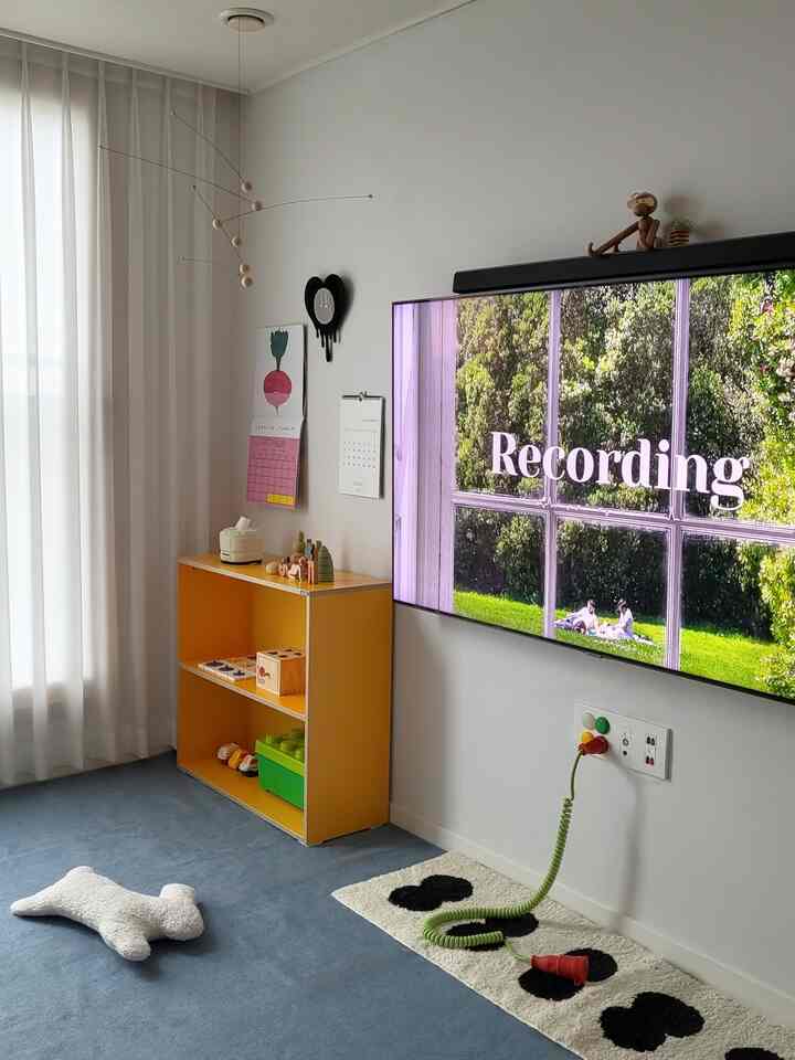 白と黄色の調和が感じられる子供部屋、青いラグにおもちゃ棚が置かれたシンプルなインテリア