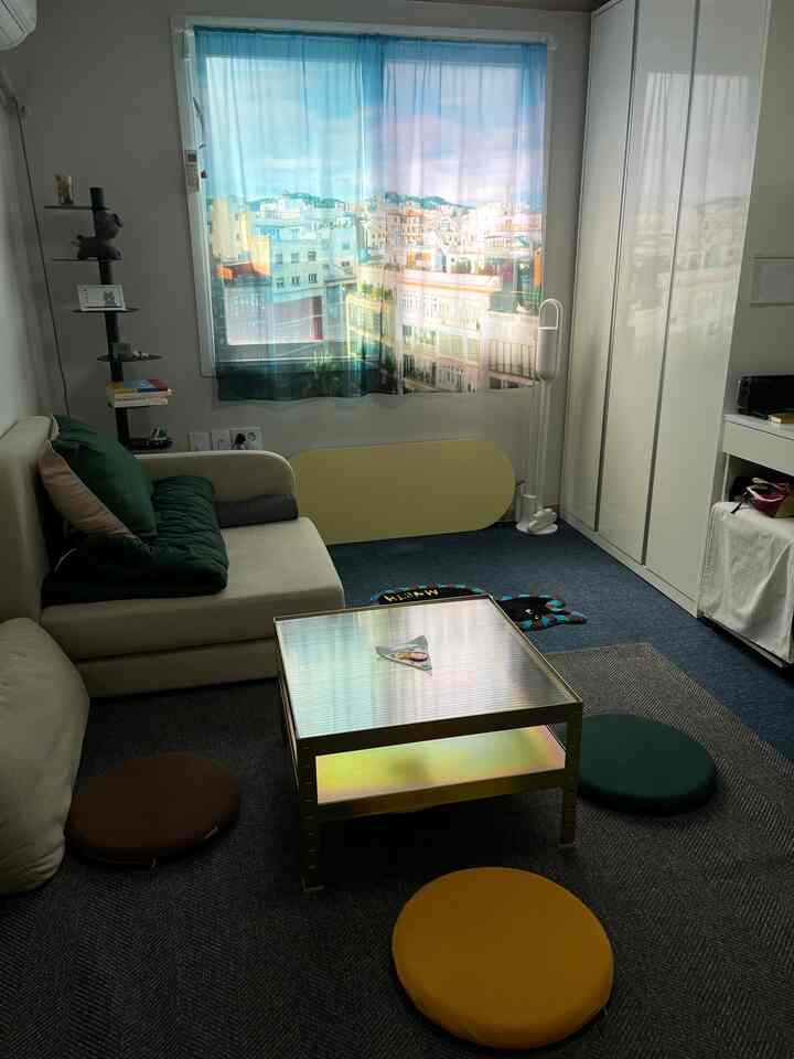 ナチュラルな色調の一人暮らし向けコンパクトリビング、ベージュのソファとカラフルなフロアクッションが配置された居心地の良い空間