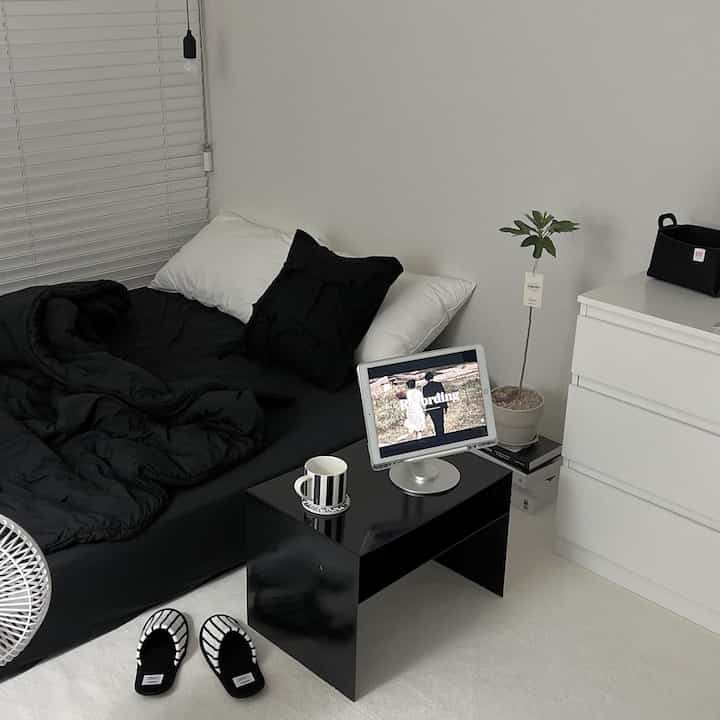 Modern black and white toned bedroom featuring bed, blinds, small table, and room slippers in a tidy space