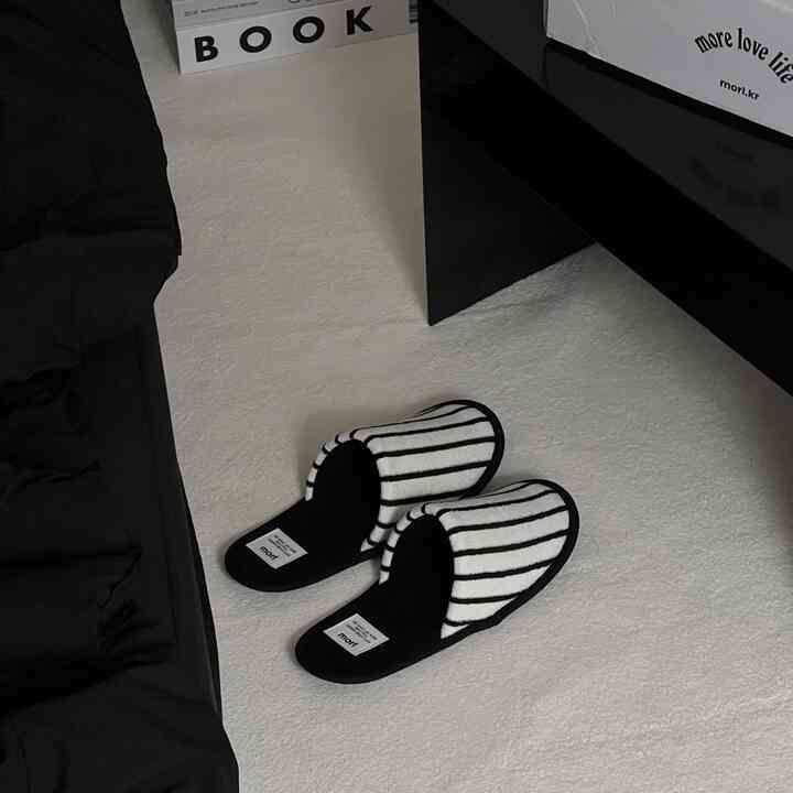 Minimal living room with white flooring and black sofa featuring striped room slippers placed centrally on the floor