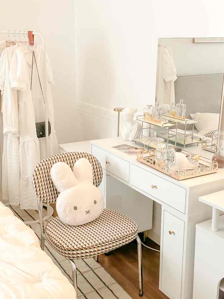White-toned bedroom featuring vanity, patterned chair with plush cushion, and rug creating a cozy atmosphere