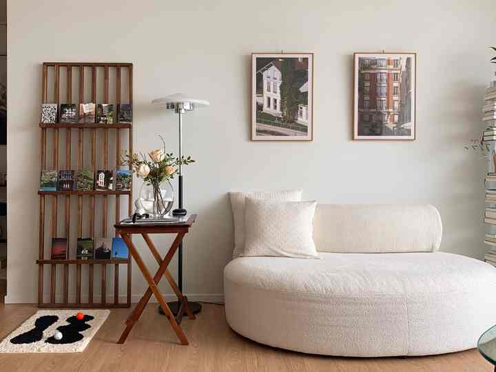 Living room with natural colors and wood tones featuring an ivory curved sofa, wooden shelves, floor lamp, and framed pictures in a simple cozy setting