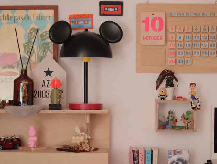 白い壁と木目調の棚が調和した空間、ミッキーマウス風のテーブルランプやレゴ多肉植物、イケア造花が配置されたミニマルで印象的なインテリア