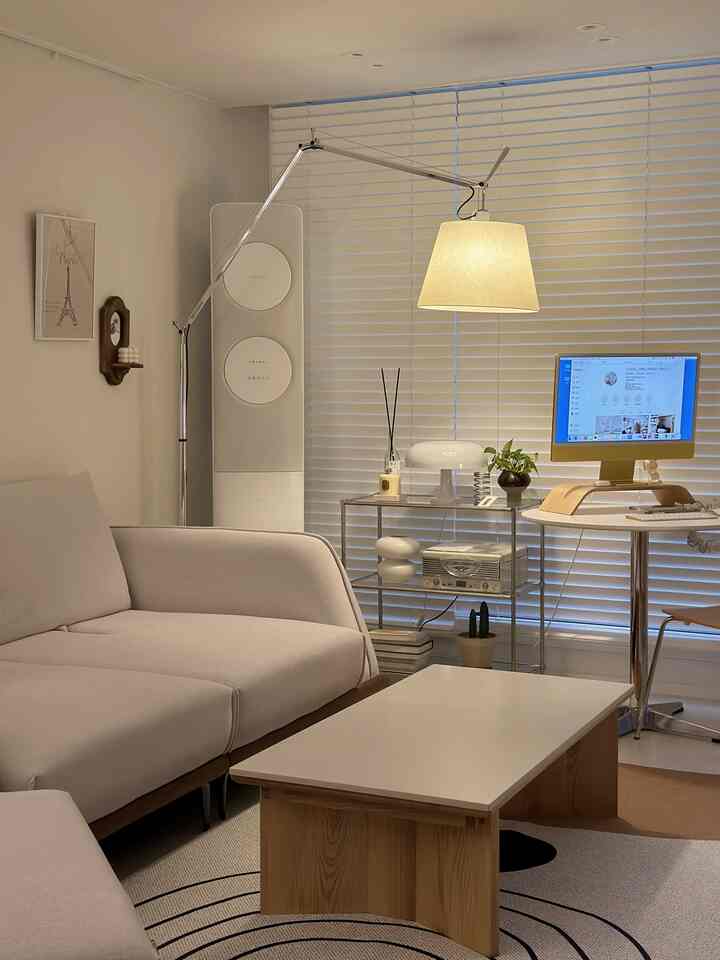 Modern living room in white and wood tones featuring sofa, coffee table, floor lamp, and a cozy home office setup