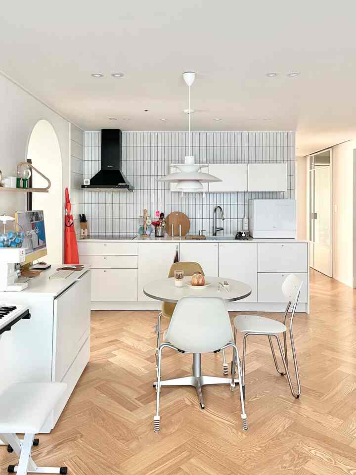 Minimal kitchen space in white and wood tones featuring a central dining table and chairs with clean, modern atmosphere