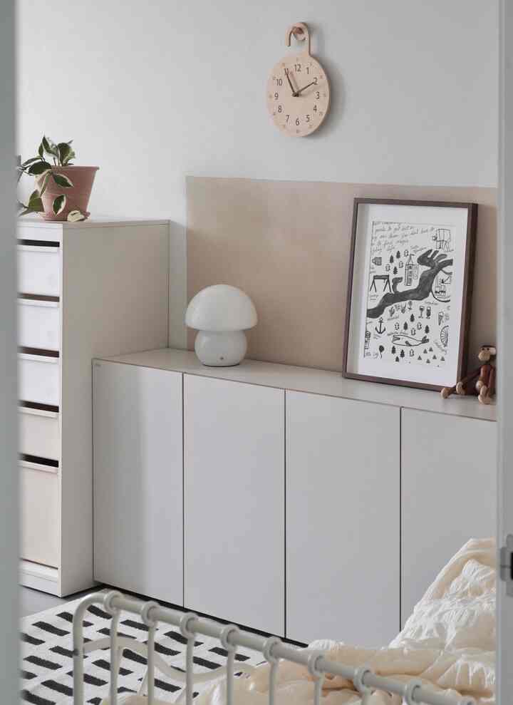 白とベージュの色調の子供部屋、すっきりとしたキャビネットとベッドフレーム、自然素材の装飾が配置された落ち着いた雰囲気のインテリア