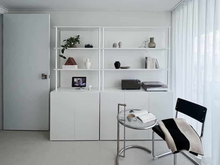 Bright white-toned tidy study space featuring lower cabinets and upper shelves with organized decor