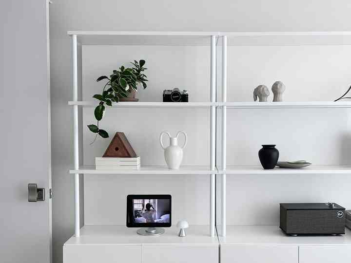 Modern white-toned shelving unit featuring plants, decorative objets, and a table lamp in a clean setup