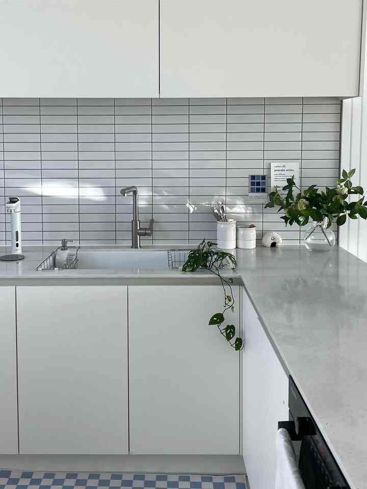 明るいホワイト調のキッチン、タイルの壁面と造花が配置された清潔でモダンなインテリア