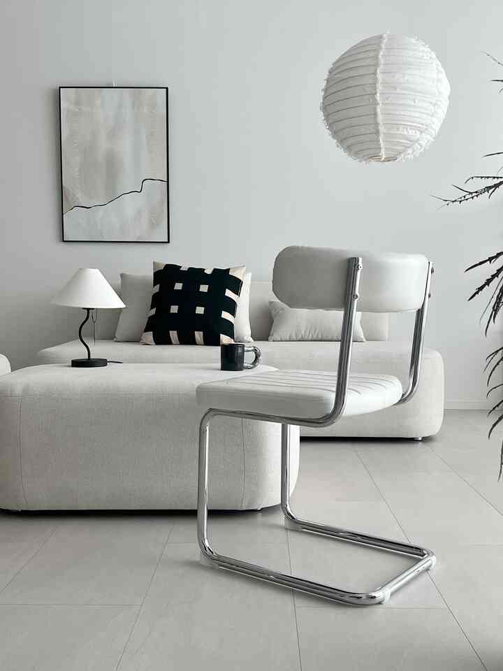 Warm white-toned living room featuring cream sofa and steel frame white chair in a minimal, modern setting