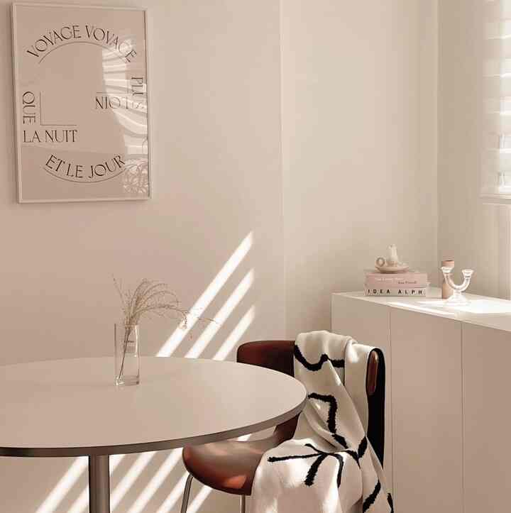 Ivory-toned walls with a round white dining table, brown chair, and black-striped blanket in a minimal dining room interior