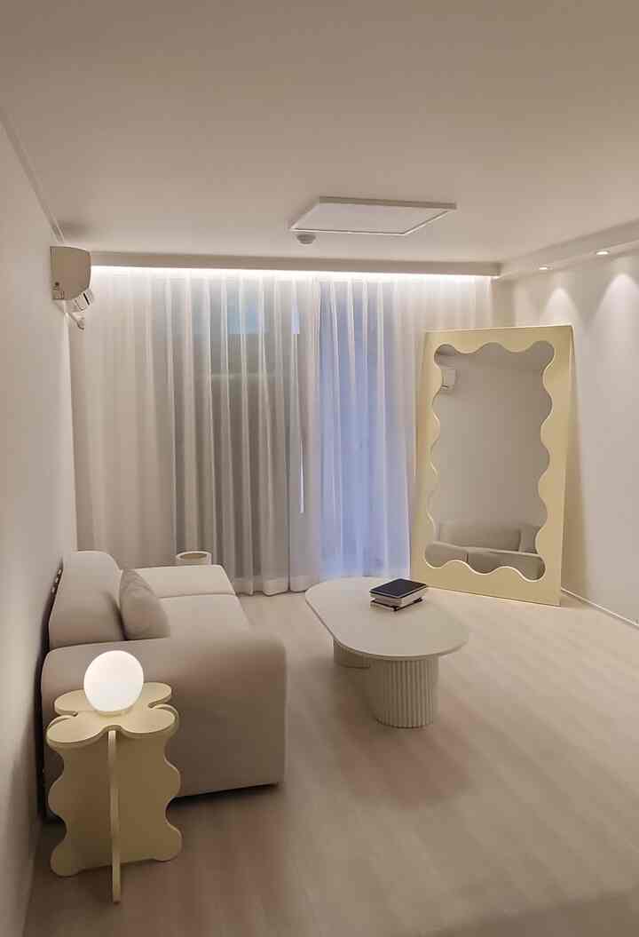 白とベージュの色調のリビング、シンプルなソファと独特なデザインの鏡、コーヒーテーブルが配置されたミニマルで雰囲気のあるインテリア