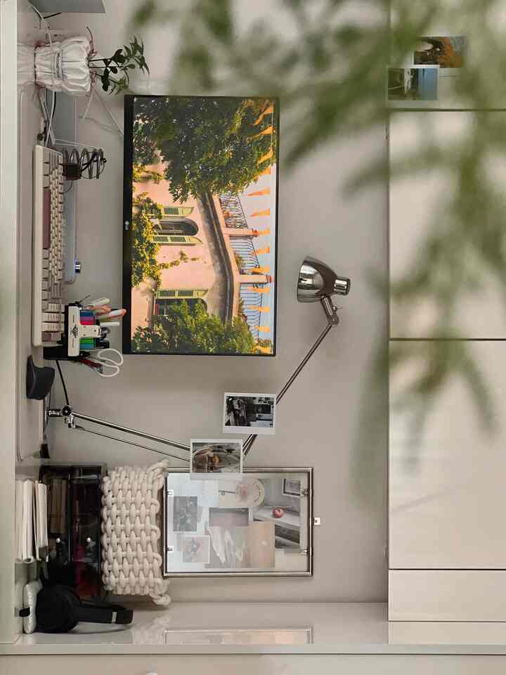 白とグレーのトーンが特徴的なシンプルなホームオフィス、デスク上にモニターとライト、額縁が配置された落ち着いた空間