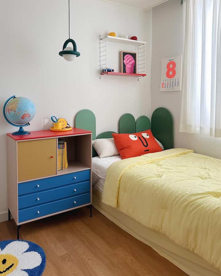 明るい黄色の寝具と緑のヘッドボードが配置された子供部屋、木目調の床とカラフルな収納が印象的なアットホームな空間