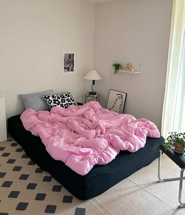 Bedroom featuring pink comforter and black mattress cover with modern, simple atmosphere