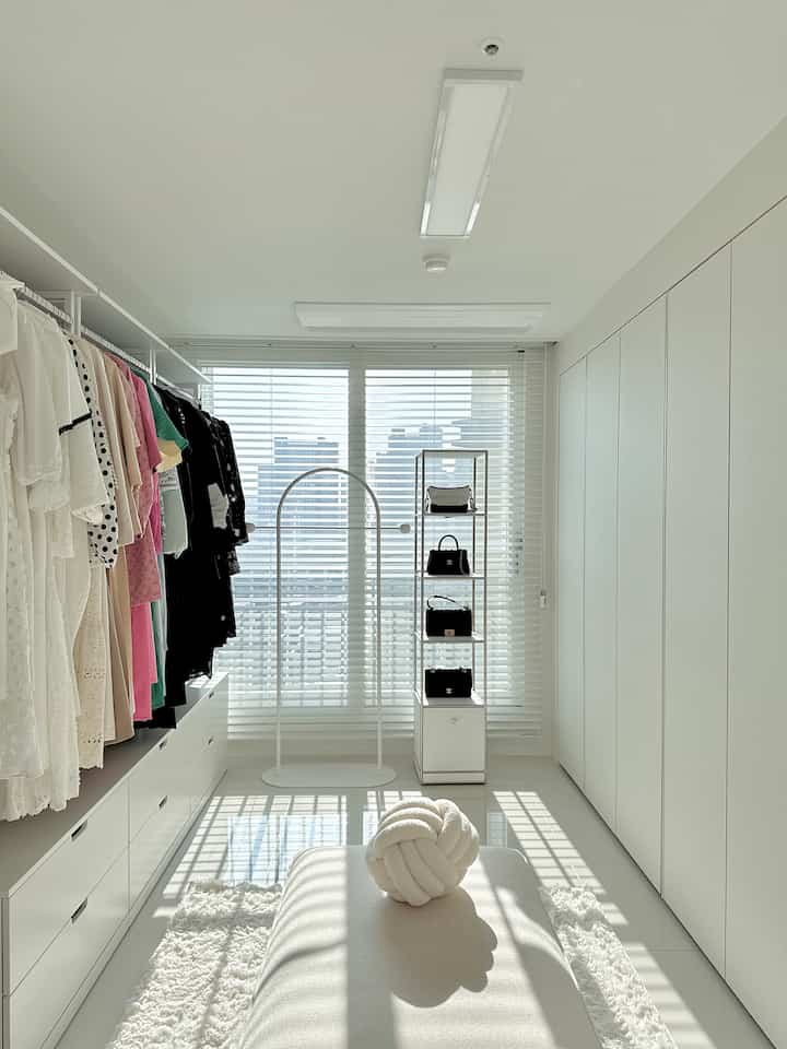 White and natural tone walk-in closet featuring built-in cabinets, hangers with organized clothes and bags in a clean space