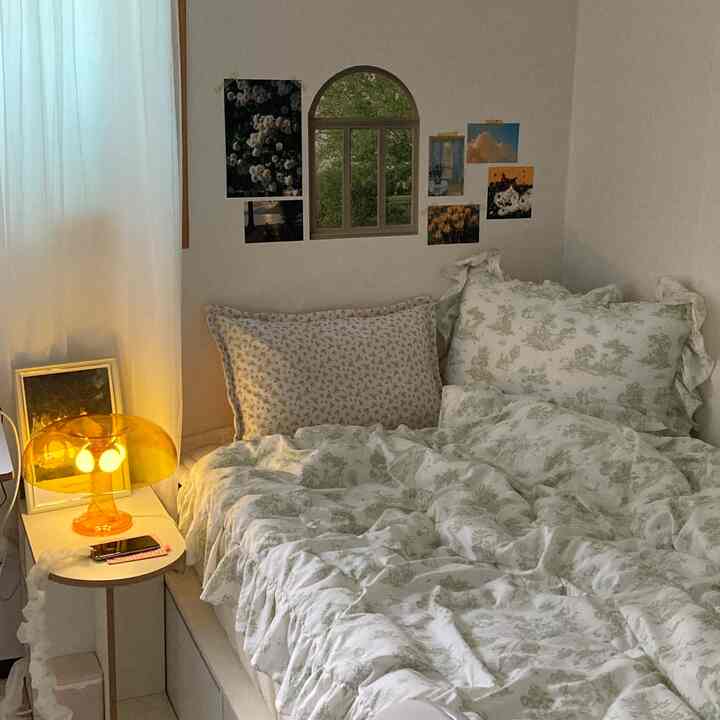 Cozy bedroom with warm yellow lighting and white bedding, featuring floral and nature posters on walls