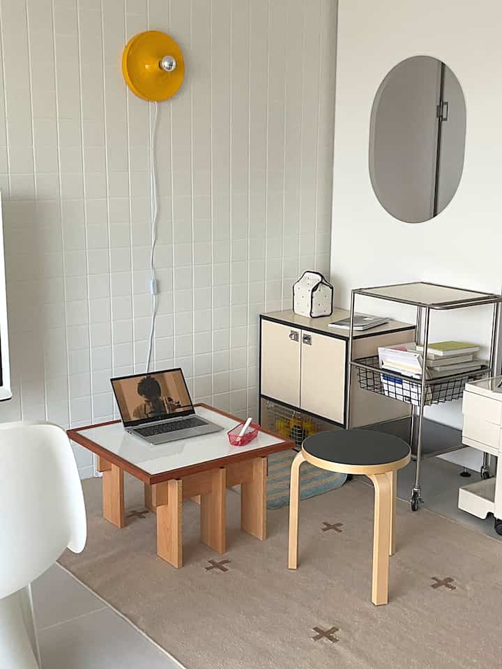 バターイエローとウッドトーンが調和したミニマルなホームオフィス、スツールとキャビネットが配置された整った空間