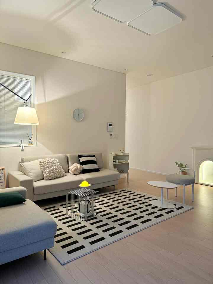 Bright white-walled living room with wood tone flooring, gray sofas, black-and-white patterned rug, featuring a minimalist modern atmosphere