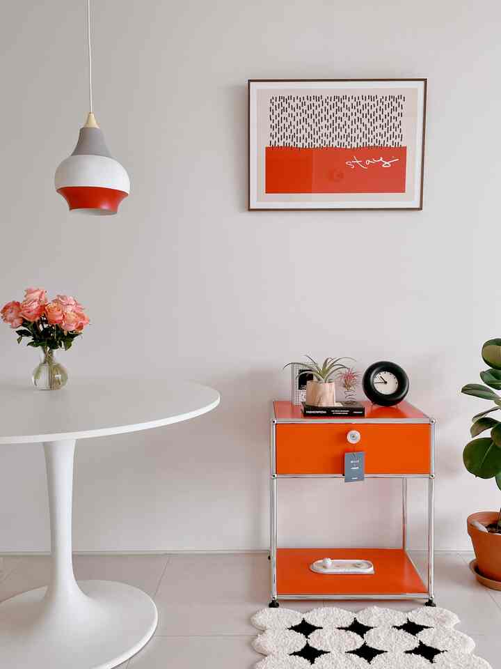 白とオレンジのトーンが際立つキッチン、楕円形のテーブルとオレンジのサイドテーブル、独特なデザインのペンダントライトが配置されたすっきりとした空間