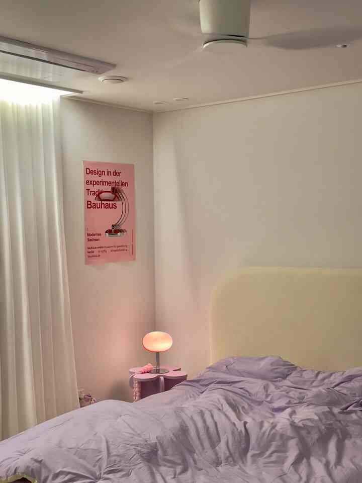 白い壁とカーテンを背景に紫色の寝具とナイトテーブルランプが配置された雰囲気のある寝室