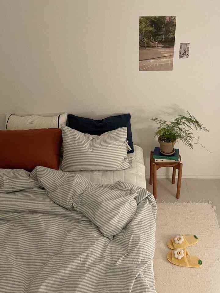 ナチュラルなホワイトの壁と木目調スツール、ストライプの寝具が配置された雰囲気のある寝室