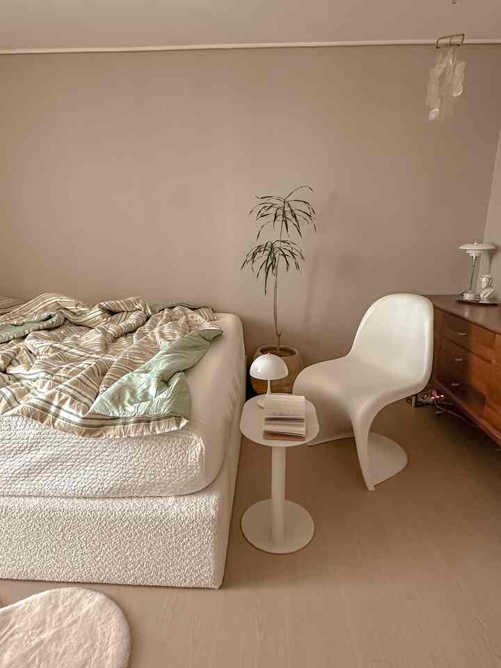 Beige and white toned bedroom featuring a Pantone chair, side table, and plant in a cozy natural modern setting