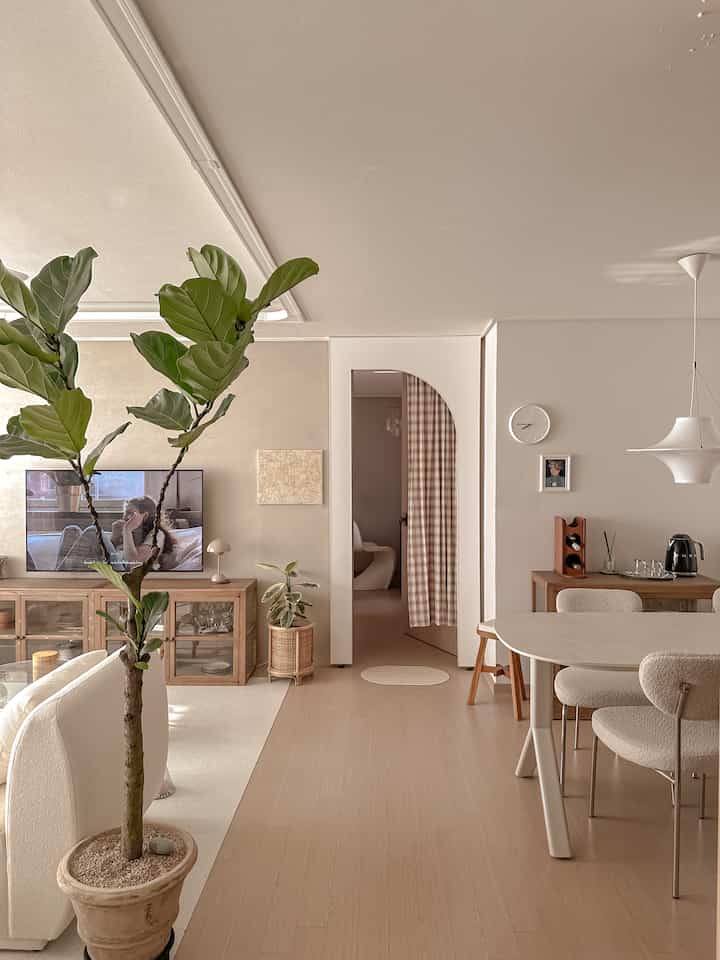 Ivory and wood tone living room with dining table, natural ambiance highlighted by arched doorway and indoor plant