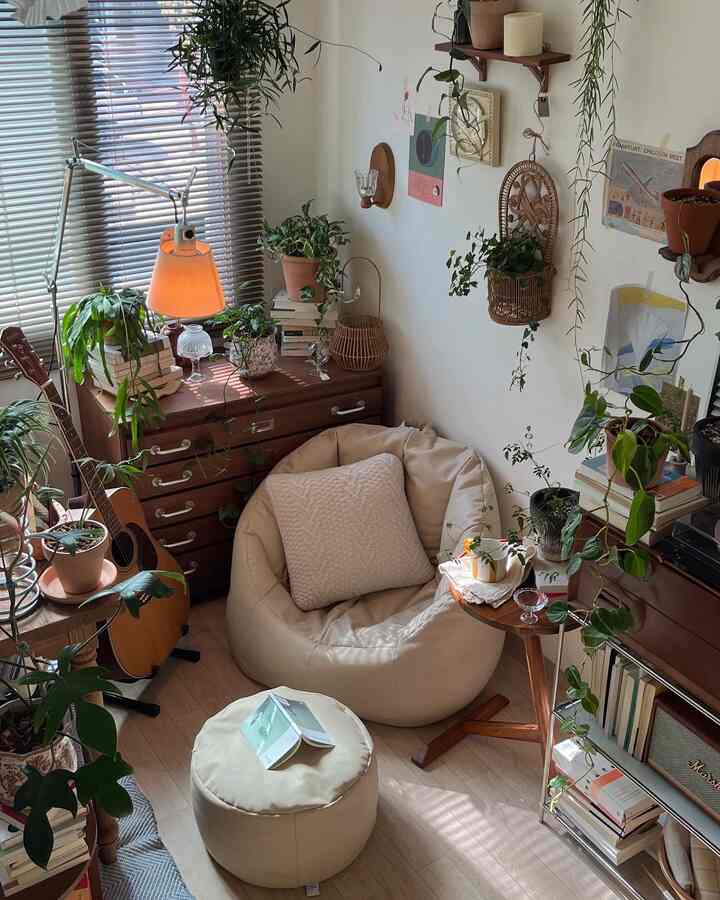 ベージュとナチュラルカラーの小さなリビング、ビーンバッグとスツール、木製チェスト、ラタンのインテリア小物、多数の植物が配置された落ち着いた空間