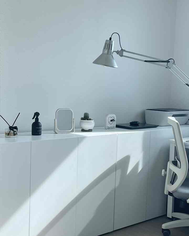 白とグレーの色調のコンピュータールーム、チェストの上にディフューザー、サボテン、照明が配置された清潔で現代的なインテリア