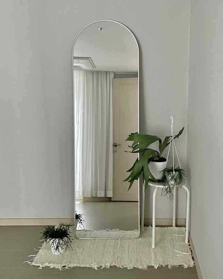 白と緑の色調が調和した寝室のコーナー、全身鏡と植物スタンドが配置されたシンプルで自然な雰囲気のあるインテリア