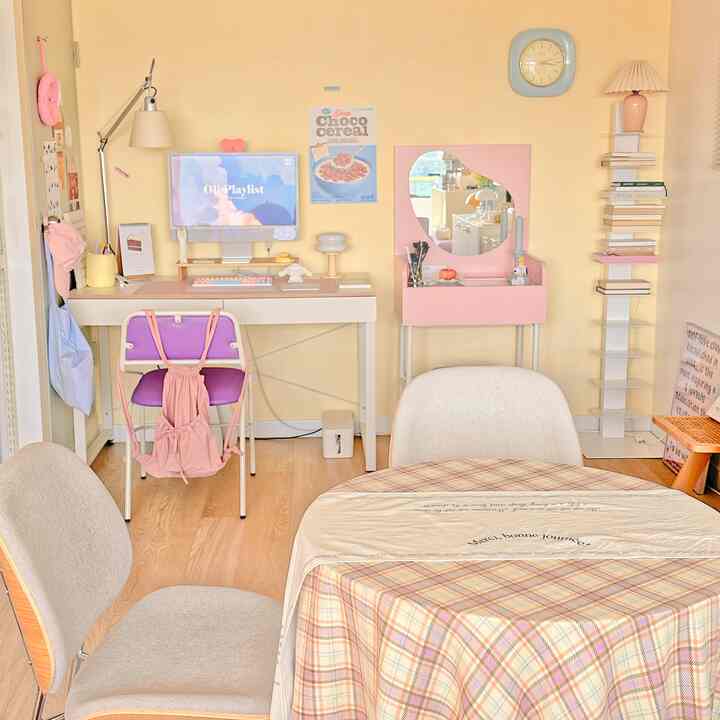 明るい黄色い壁にピンクの小物が配置されたホームオフィス兼ダイニングルーム、ナチュラルなベージュ色の椅子とファブリックのテーブルが雰囲気のあるインテリア