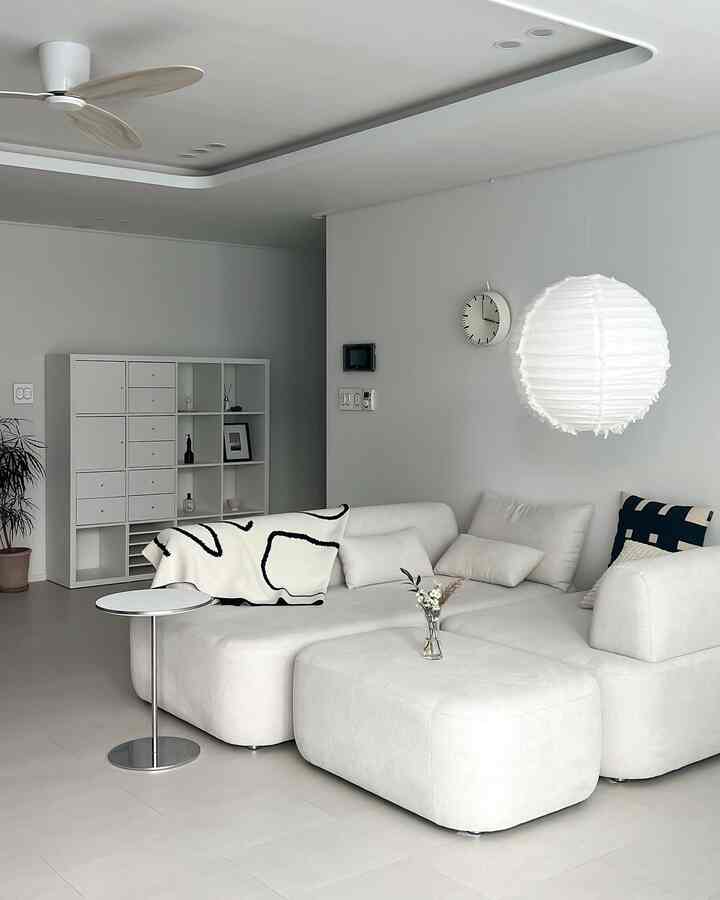 White-toned living room featuring a modern sectional sofa, pendant light, and simple side table with a cozy atmosphere