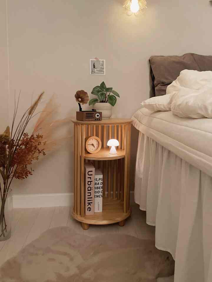 Bright natural wood-tone bedroom featuring a wooden cylindrical nightstand, bed, table lamp, and clock creating a warm atmosphere
