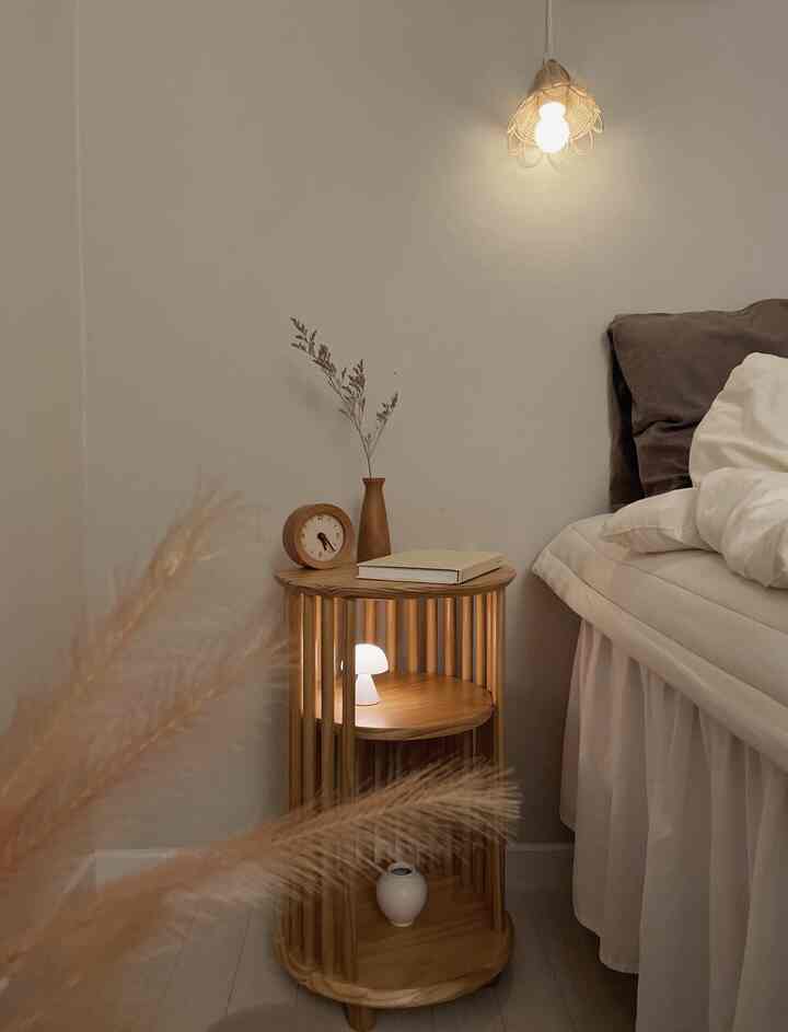 A white and wood-toned bedroom featuring a wooden nightstand with lighting, creating a simple and natural atmosphere