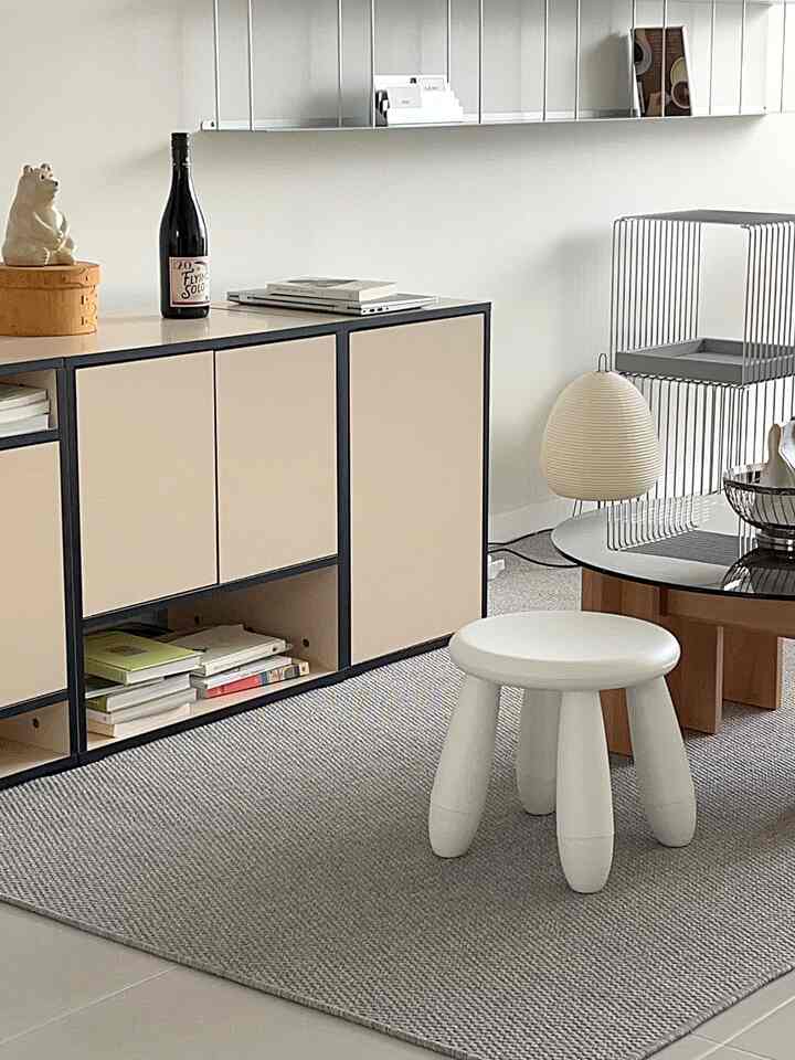 ベージュとグレーの色調のリビング、ベージュのキャビネットと白いスツールが配置されたミニマルな雰囲気のインテリア