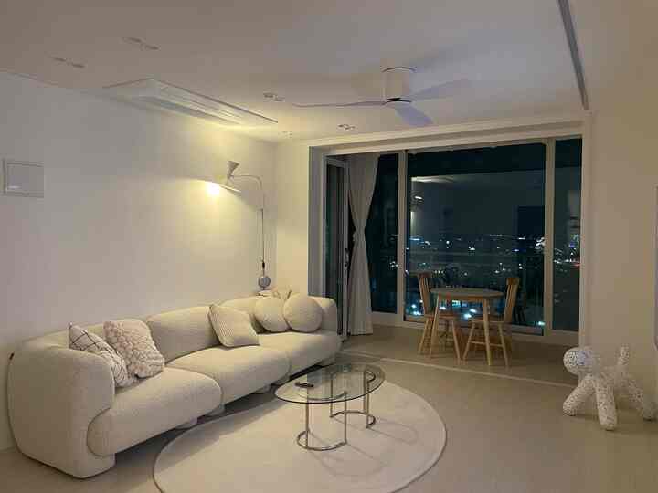 白を基調としたリビング、曲線的なソファとガラスのコーヒーテーブル、木製のダイニングセットが置かれた印象的な空間