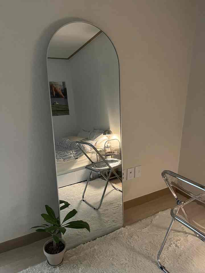 Ivory-toned walls and floor with transparent folding chair and large full-length mirror in a minimal bedroom space