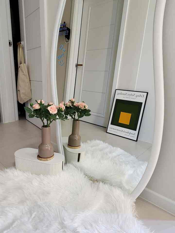 白とベージュのトーンの玄関、波形の大きな鏡と白いラグ、花瓶が配置されたモダンな雰囲気のインテリア