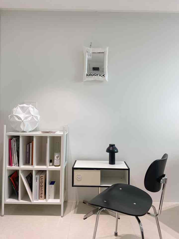 A small study space in white and black tones featuring a bookshelf, side table, and simple modern atmosphere