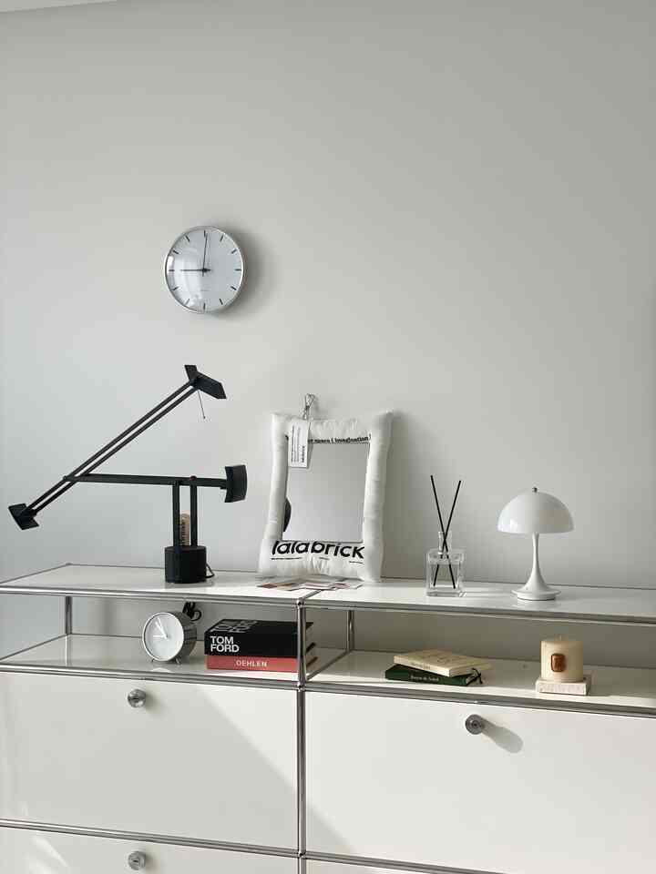 Minimal white-toned living room featuring a console with table lamp, diffuser, and clock, creating a clean and serene atmosphere