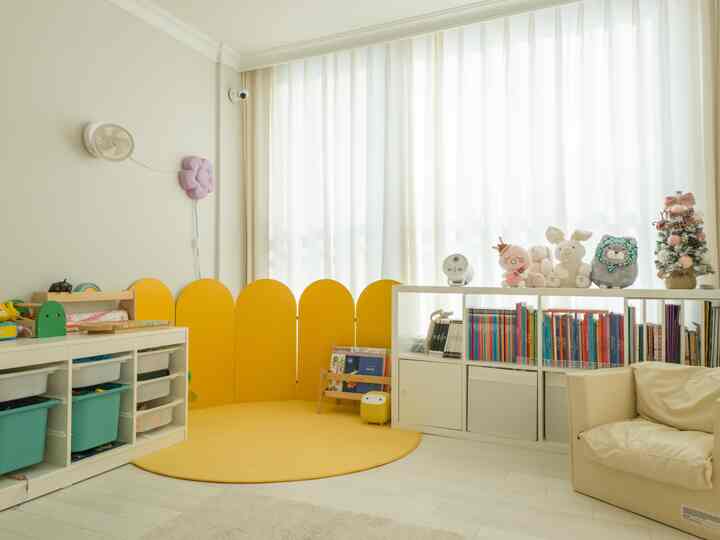 明るいホワイトとイエローの色調の子供部屋、多様な収納家具とラグ、ぬいぐるみが配置された温かみのあるインテリア