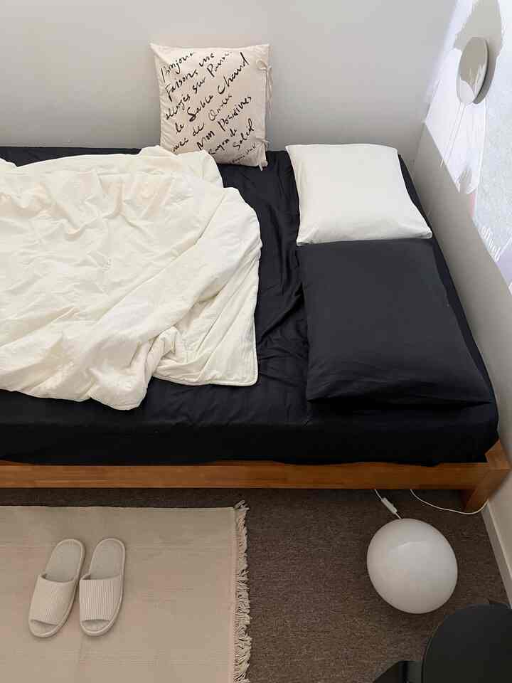 ナチュラルトーンの寝室、ウッド調のベッドに黒いマットレス、枕とブランケットが快適に配置された空間