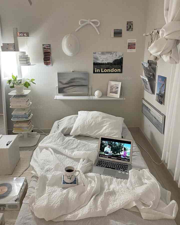 White and beige toned studio bedroom featuring a bed, bookshelf, and wall decor with a cozy atmosphere