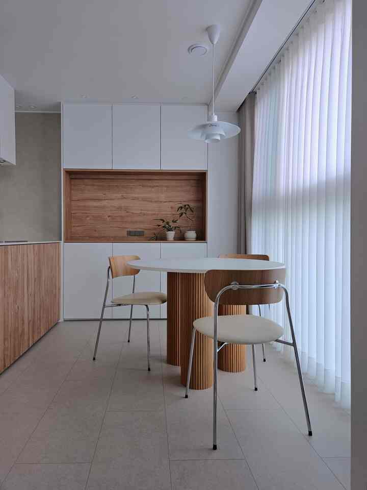 Minimal modern kitchen featuring white and wood tone round dining table with chairs, creating a cozy atmosphere