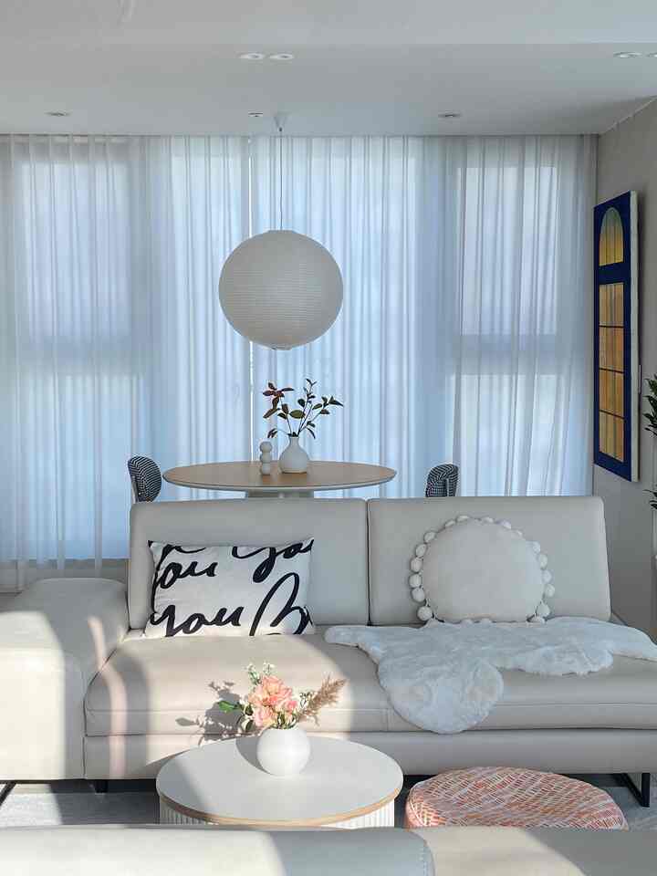 Bright white-toned living room featuring a round wooden table, beige sofa with lettering and round cushions in a simple modern style