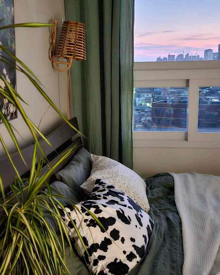 Green and natural toned bedroom featuring plush bedding and pillows next to a window, creating a cozy atmosphere