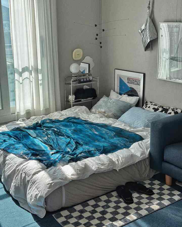 ブルーと白のトーンの寝室、ミッドセンチュリーモダンのベッドとソファ、ポスターが配置された印象的な空間