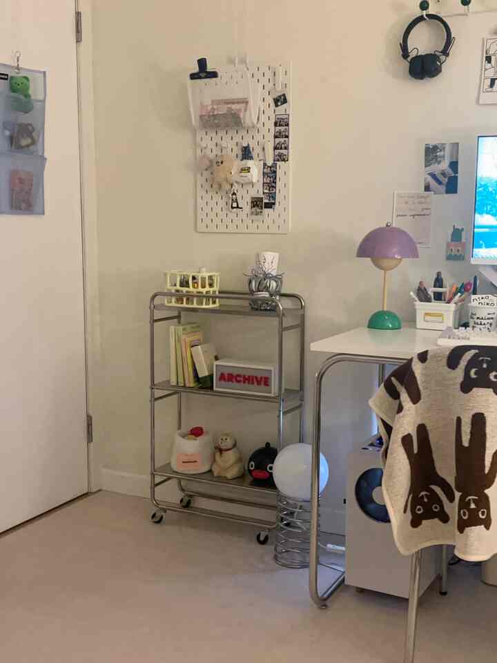 ホワイトトーンの狭い部屋にミッドセンチュリーモダン風のデスクと収納用メタルトロリーが配置された雰囲気のあるホームオフィス